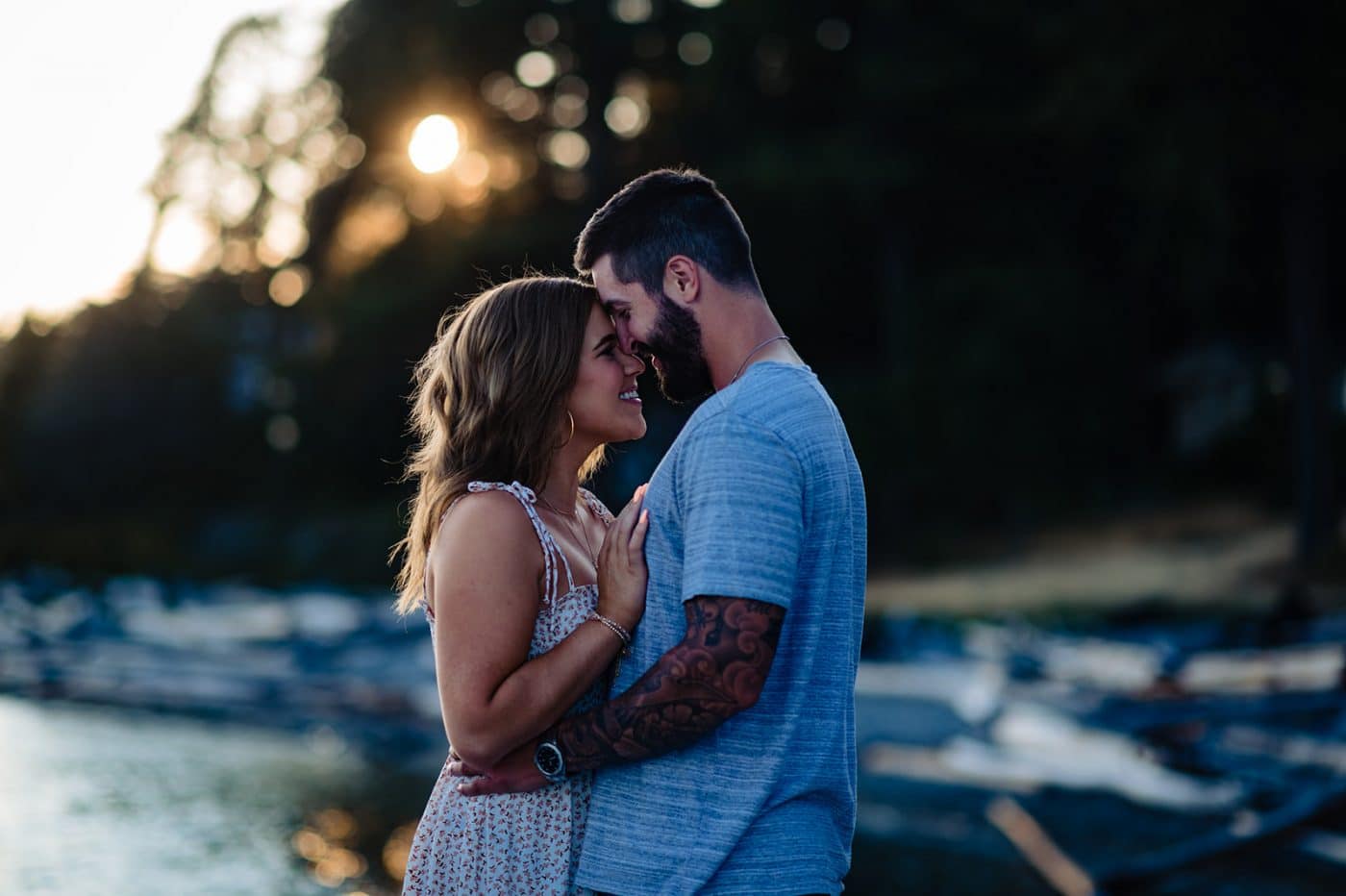 newly engaged couple enjoys the sunset as she lays her forehead against his face and they smile after their surprise proposal
