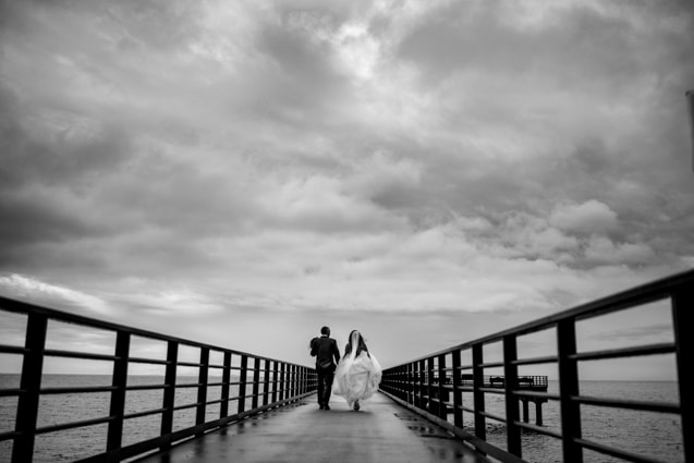 fresh  air photography pricing helps you afford to document your big days and everyday moments to remember for years to come like this bride and groom running down a pier under stormy skies