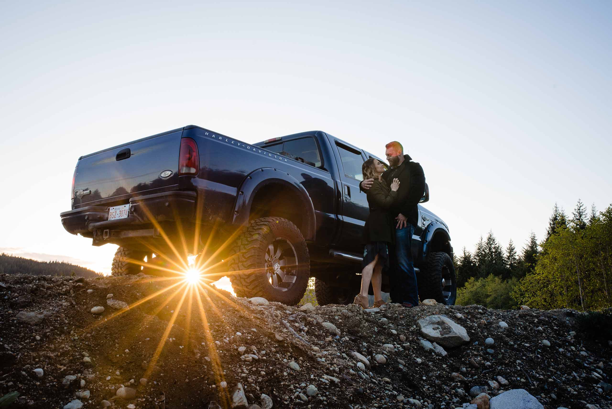 young couple poses at sunset at the Fresh Air Photography farm in sechelt next to a jacked up Harley Davidson edition pick up truck