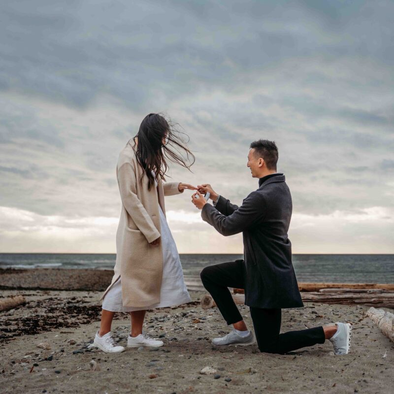 man proposing on his one knee to his partner on the sandy beach at Davis Bay on the Sunshine Coast BC