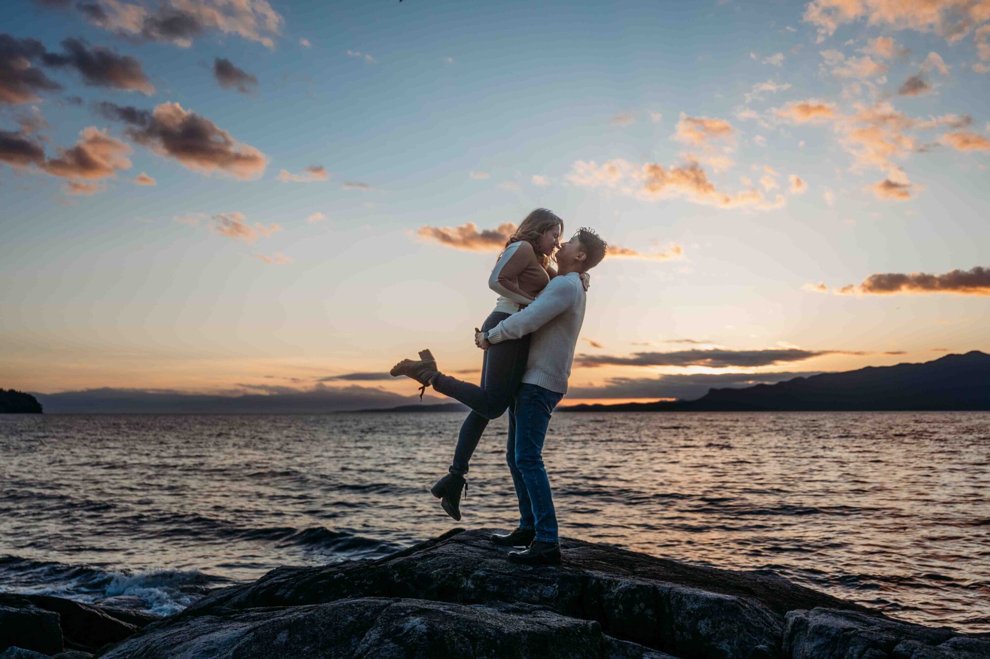 newly engage couple embrace in front of sunset
