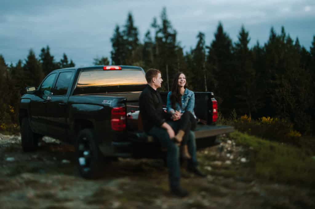 young couple sit on the back of truck and watch sunset