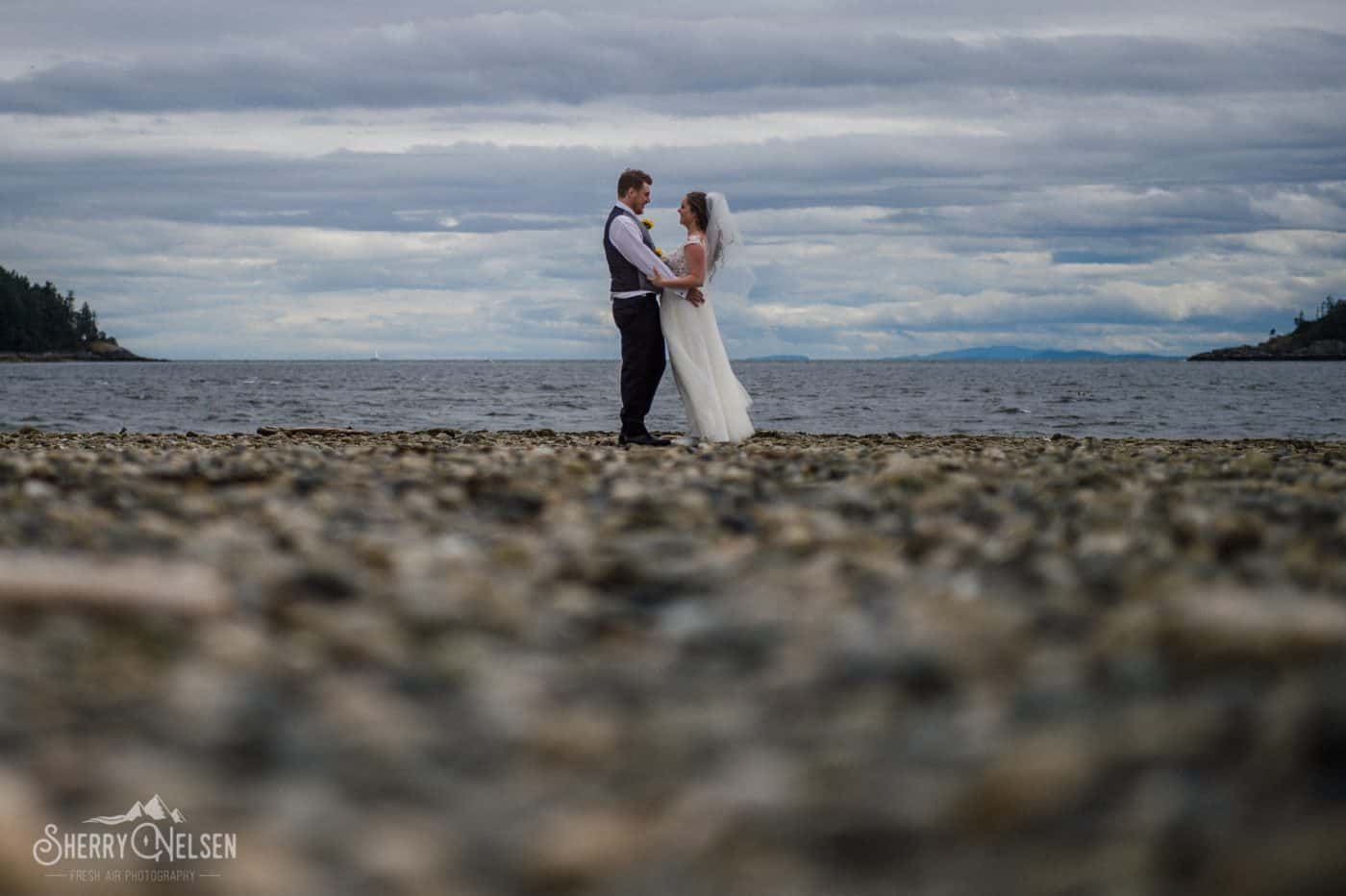Shane & Shelbi embrace along the pebbles on the beach on Wakefield Beach on their wedding day