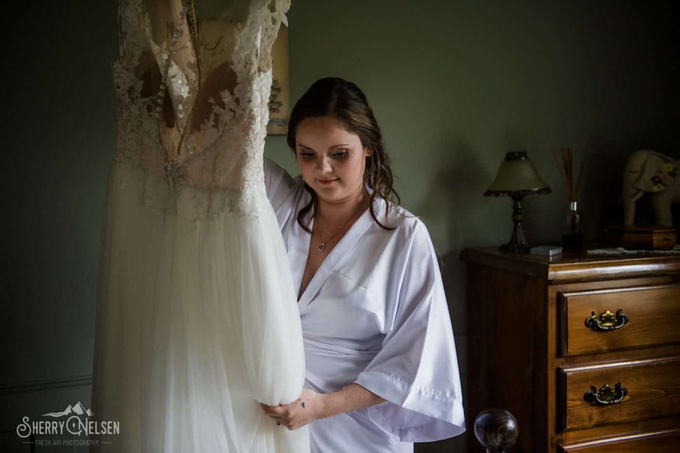bride looks at her wedding dress just before putting it on in Sechelt BC