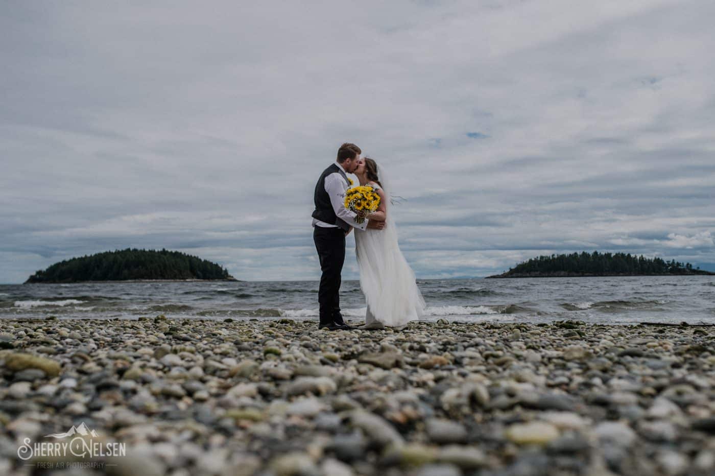 Bride and groom kiss on Wakefield Beach framed between Trail Islands