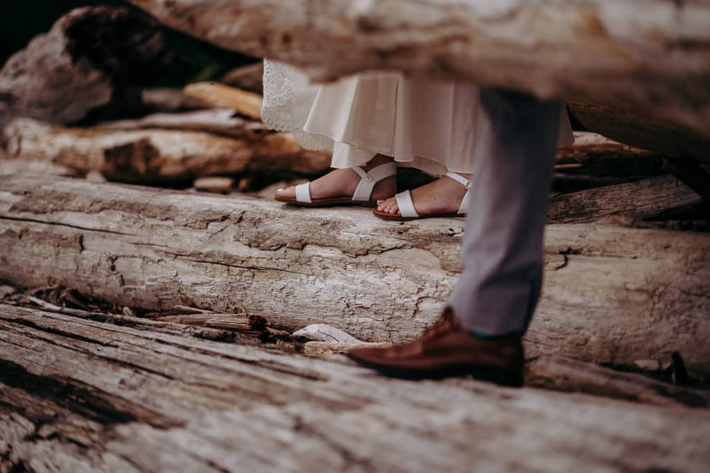 groom and bride's feet as they traverse the logs on the beach for portraits