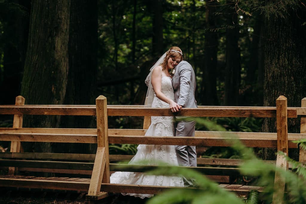 bride and groom embrace on a bridge in the forest at their Sunshine Coast BC wedding