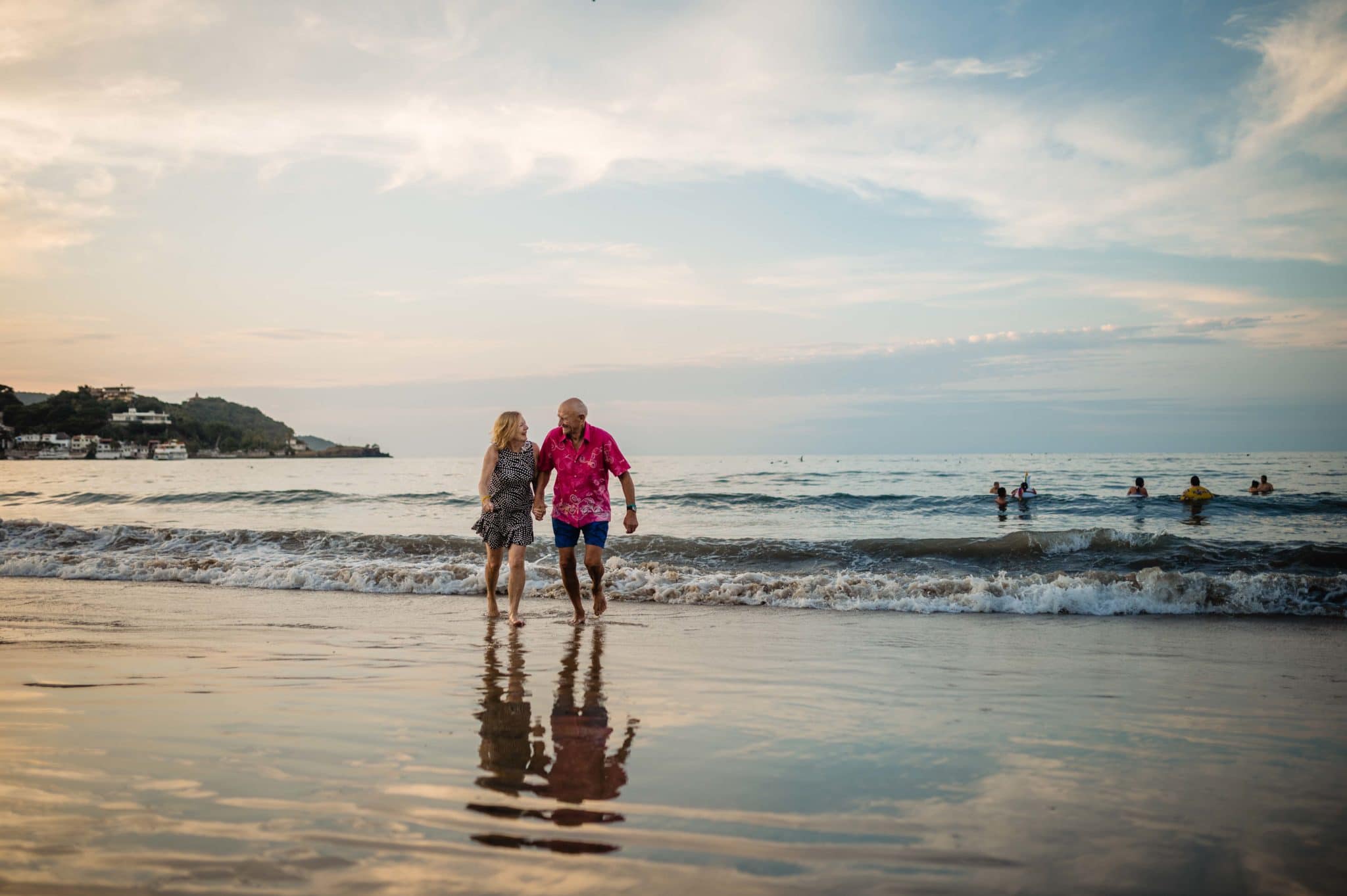 a couple who has been married for 59 years runs in the surf on a beach at sunset