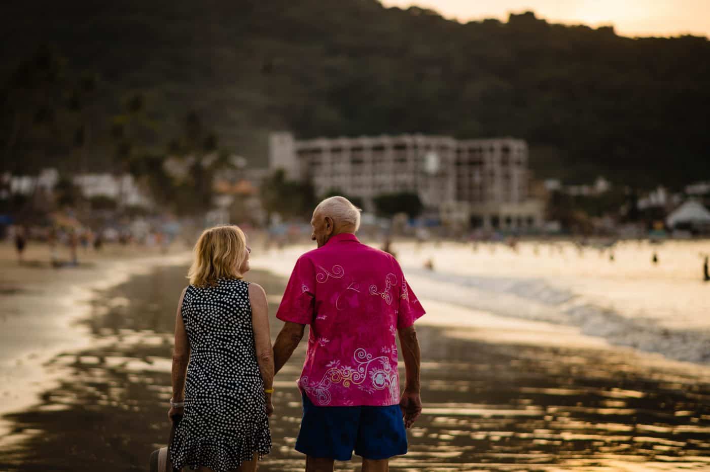 a couple who has been married for 59 years walks on the beach in Mexico at sunset
