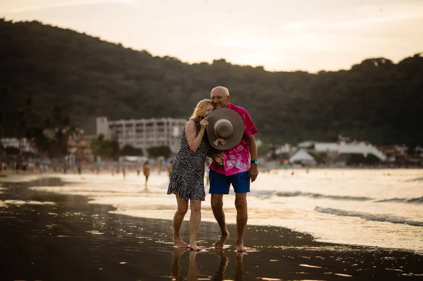 a couple who is celebrating  59 anniversary story  smiles as they walk on the beach at sunset