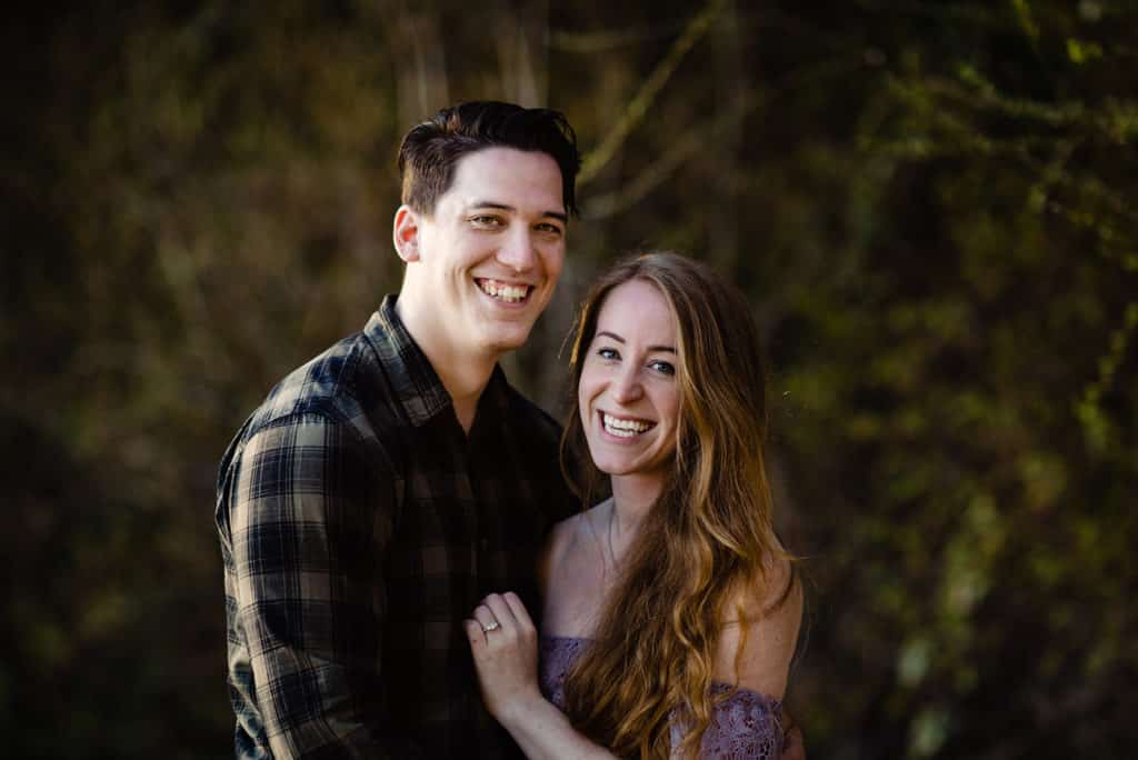 caucasian man with dark hair hugs his auburn-haired fiance and they smile for the camera right after he proposes to her in a forest in Sechelt BC. Photos by Sherry Nelsen of Fresh Air Photography