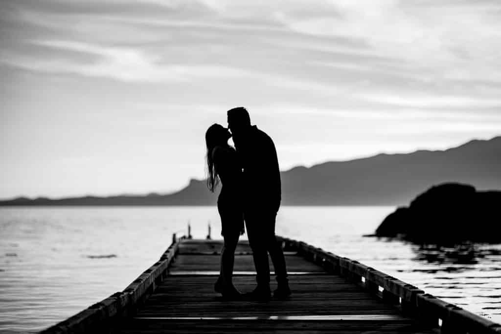 man and woman hug and kiss on a dock overlooking the ocean in this silhouette photo by Fresh Air Photography