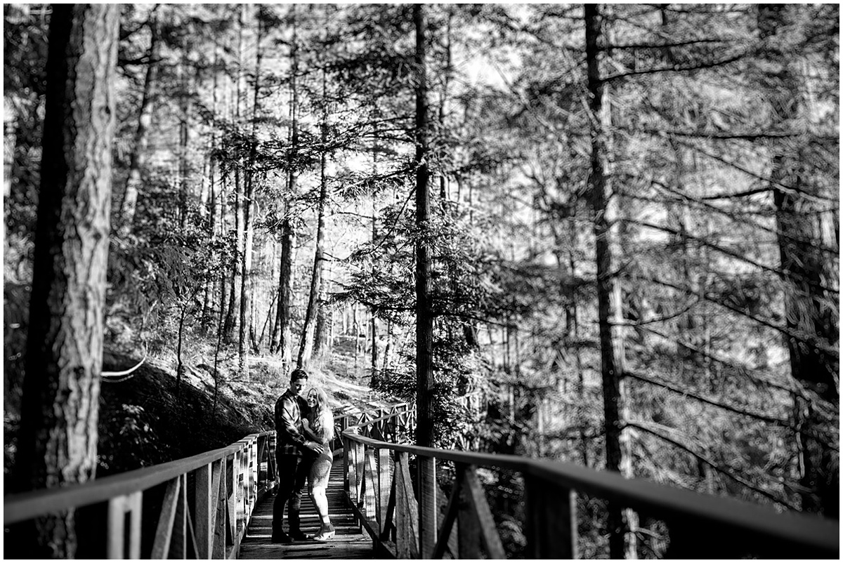black and white image of a newly engaged couple enjoying the boardwalk paths through the forest at Rockwater Secret Cove Resort in this Sunshine Coast proposal story