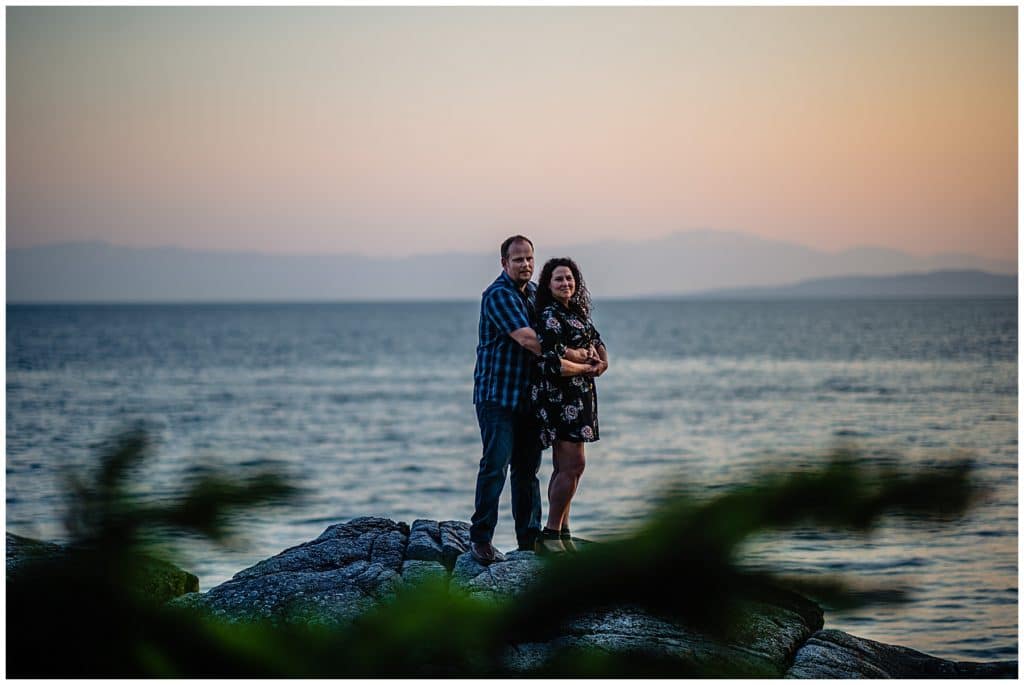 man and woman pose on a rock at sunset