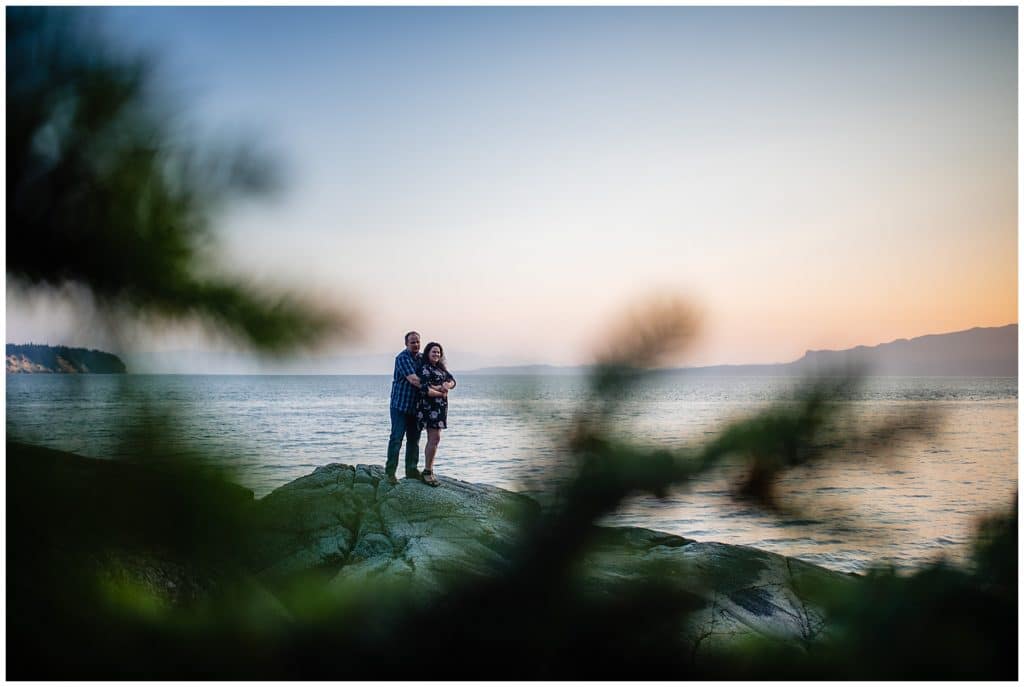 man and woman embrace on rock bluff on the ocean
