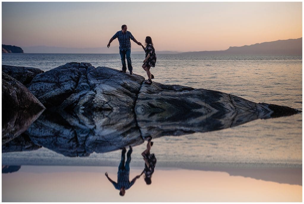 man and woman walk on rock bluff at sunset with a nice reflection