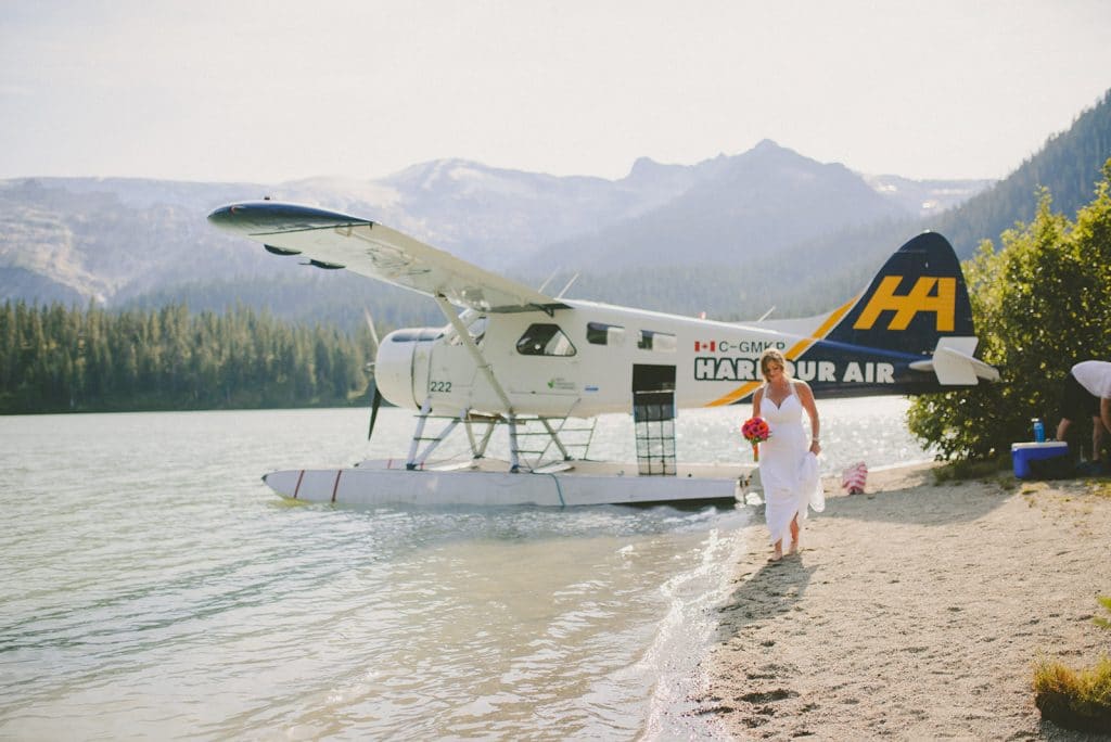 fresh air photography photographer sherry nelsen walks along the shore of a high mountain lake with a foat plane in the background during her adventure elopement in british columbia
