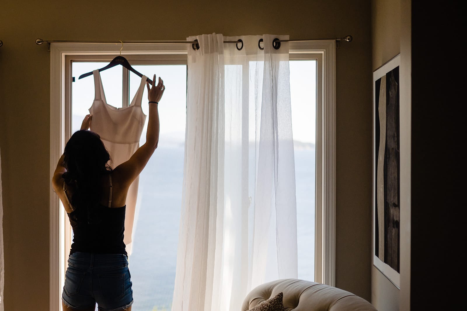 bride pulls dress down from hanging in the window to get ready for her Sunshine Coast Elopement in Halfmoon Bay