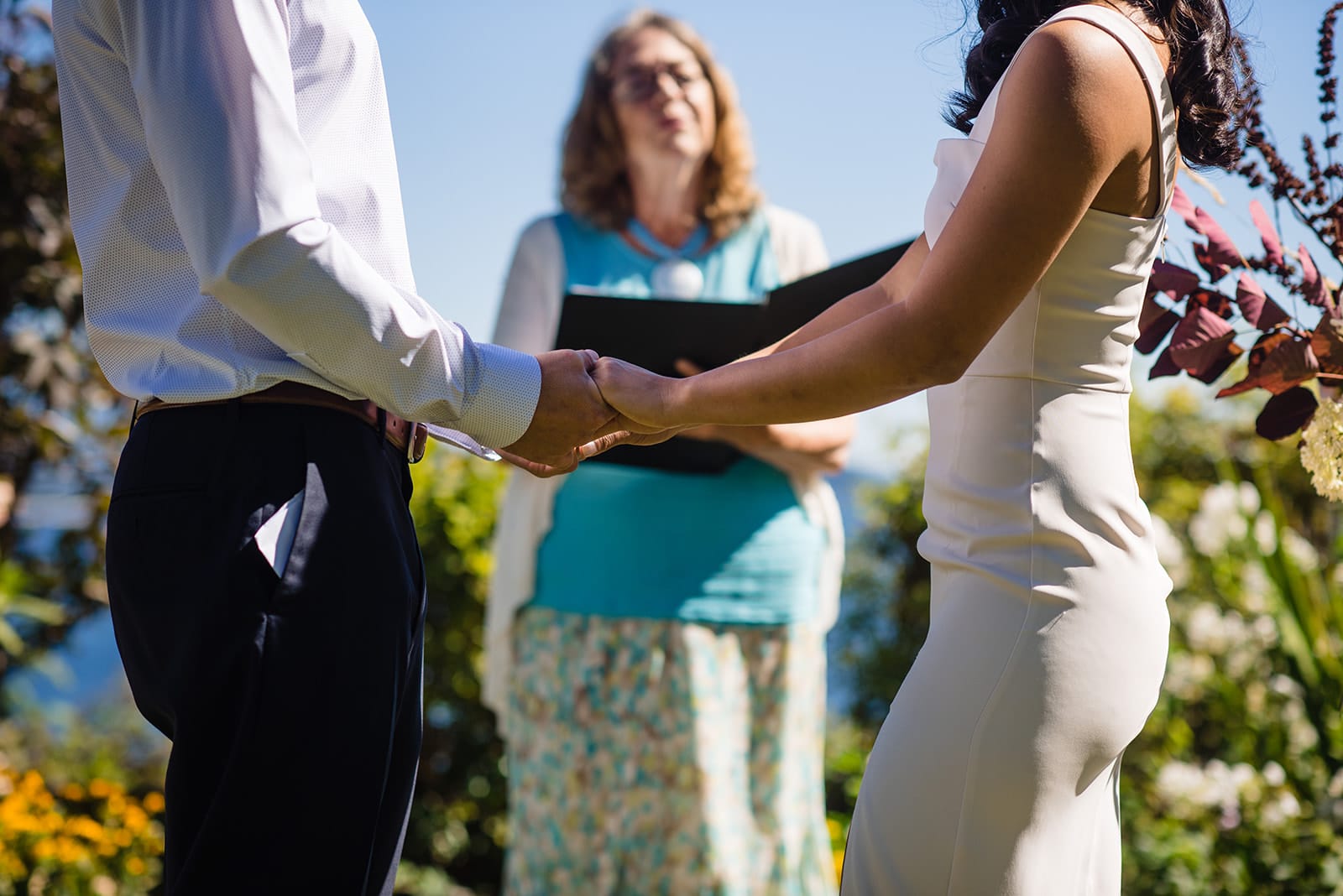 bride and groom join hands before the officiant as they marry in a private ceremony in Halfmoon Bay