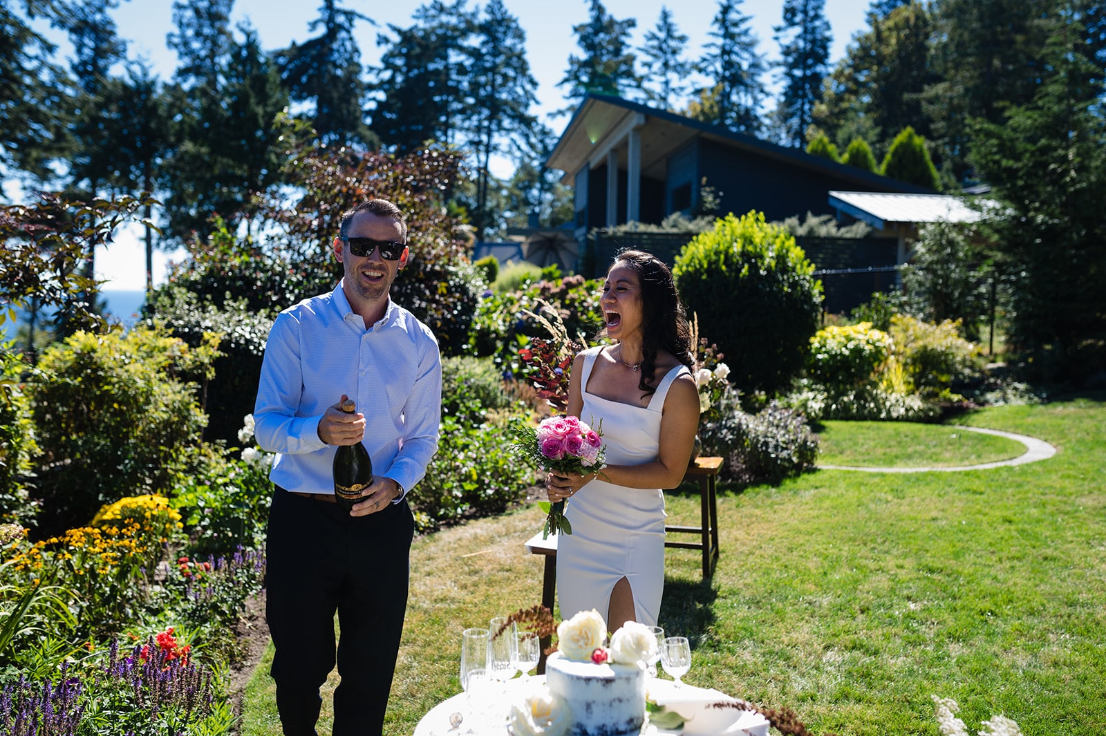 Groom pops the bottle of champagne as the bride smilles in happiness on the beautiful Sunshine Coast BC