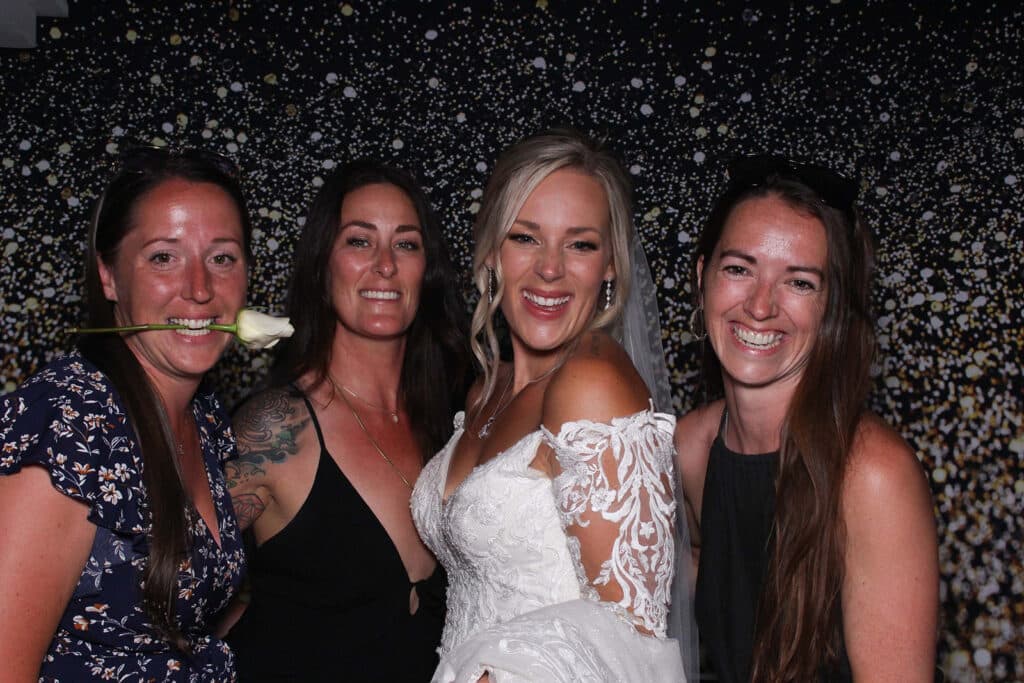 Bride in her lace wedding dress smiles at the camera next to her three friends inside her Sunshine Coast photo booth rental  