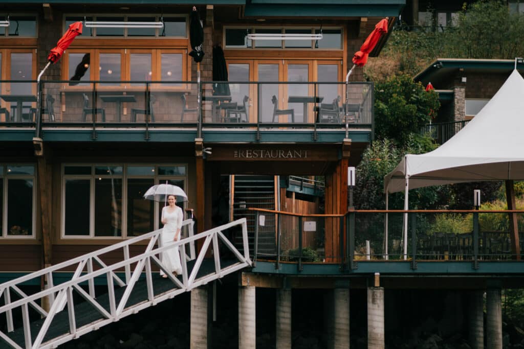 A beautiful bride stands with an umbrella outside her BC wedding venue Painted Boat Resort Spa & Marina